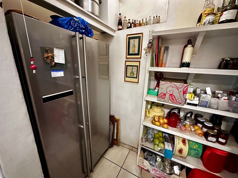 A functional scullery or pantry area featuring built-in shelving and tiled flooring, providing additional storage space adjacent to the main kitchen.