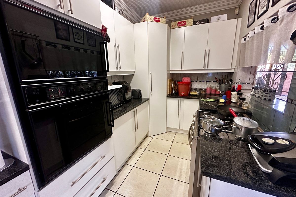 A functional kitchen featuring white cabinetry, granite countertops, a built-in oven, gas hob, and tiled flooring with a decorative ceiling finish.