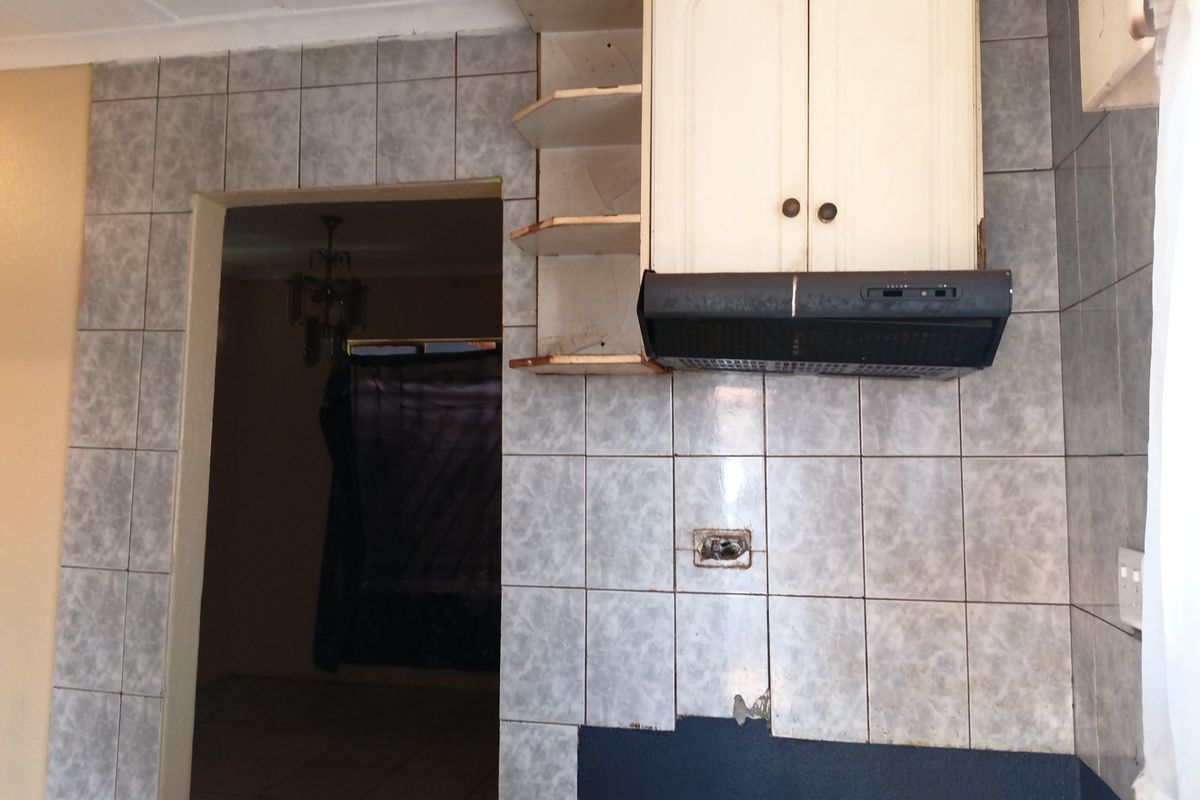 A dated kitchen area featuring tiled splashbacks, wall-mounted cabinetry, and an extractor fan, currently requiring renovation and repair to the wall finishes and electrical points.