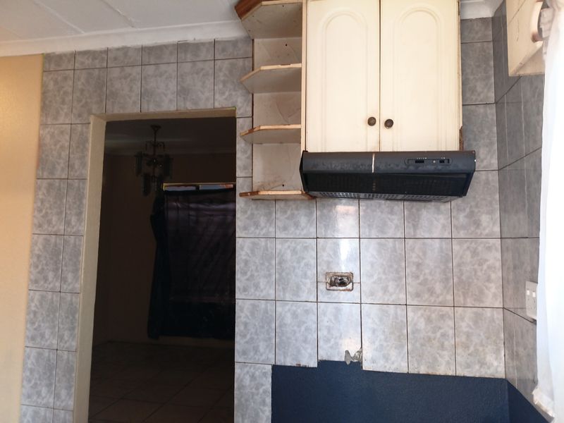 A dated kitchen area featuring tiled splashbacks, wall-mounted cabinetry, and an extractor fan, currently requiring renovation and repair to the wall finishes and electrical points.