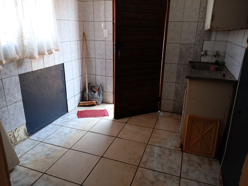 A functional laundry area featuring tiled walls and flooring with a built-in stainless steel sink and direct exterior access.