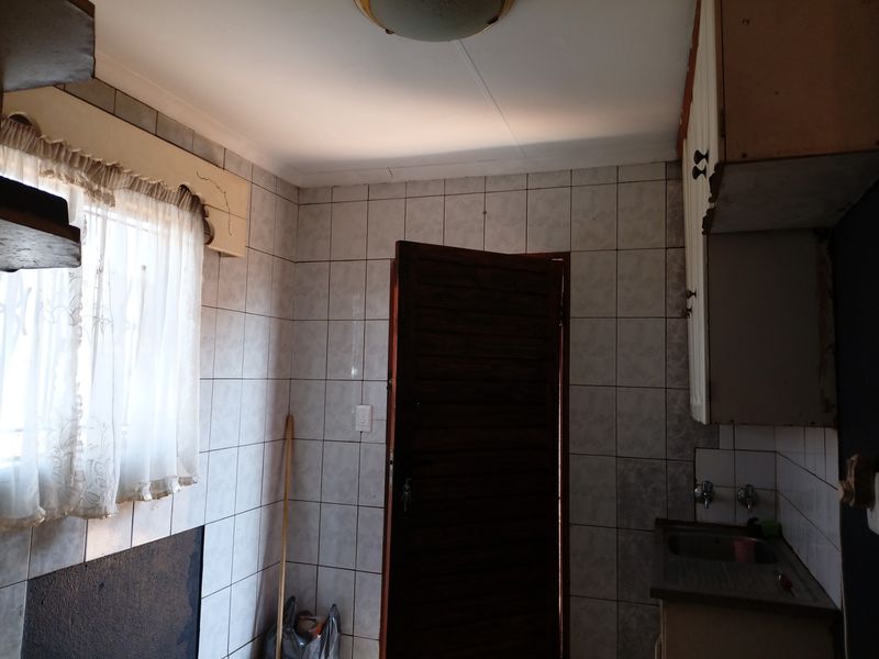 A functional scullery area featuring tiled walls, built-in cabinetry, and a stainless steel sink, offering a practical space for food preparation and cleaning.