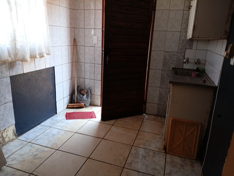 A functional laundry area featuring tiled walls and flooring, a stainless steel sink, and direct access to the exterior via a timber door.