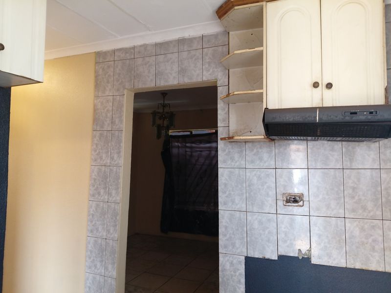 A dated kitchen area featuring tiled splashbacks, built-in cabinetry, and an extractor fan, currently requiring maintenance and cosmetic updates.