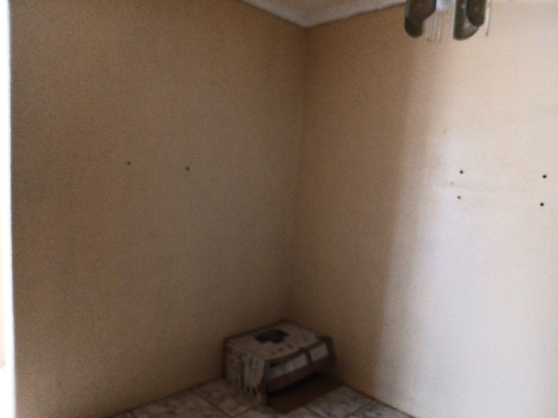 An empty bedroom featuring tiled flooring and a ceiling light fixture, currently showing signs of wall surface damage and holes.