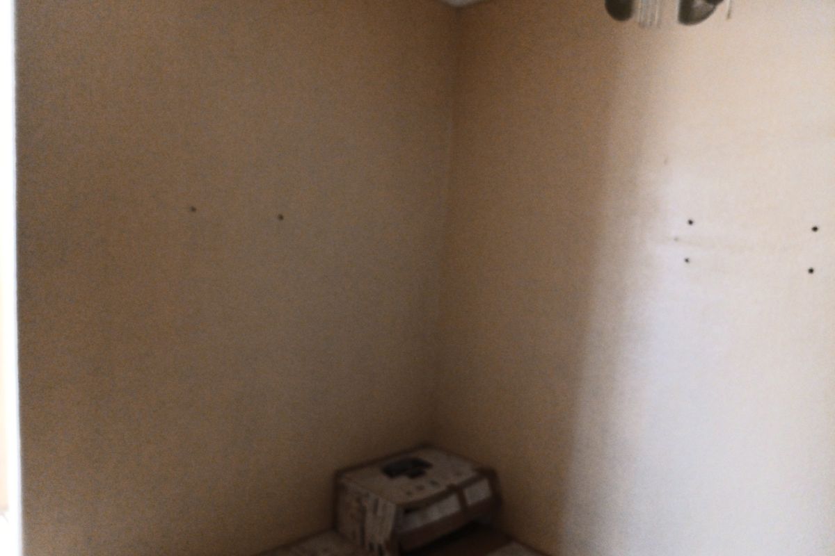 An empty bedroom featuring tiled flooring and a ceiling light fixture, currently showing signs of wall surface damage and holes.