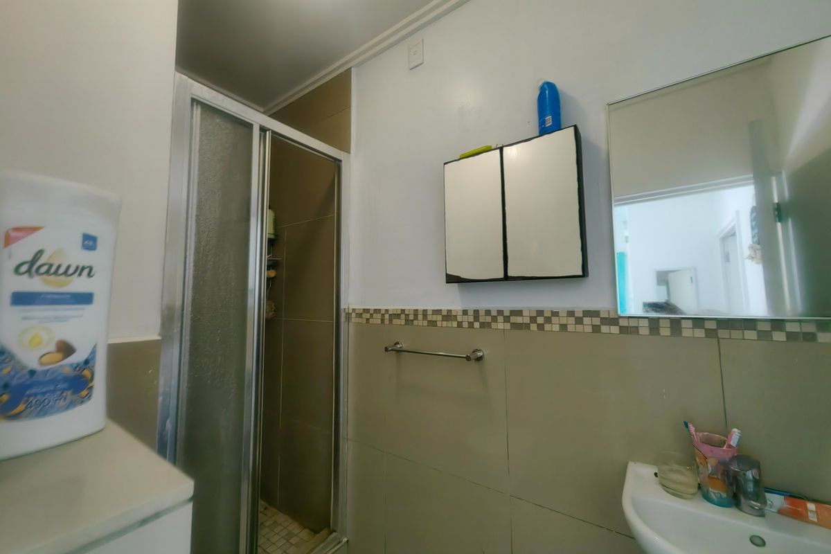 A functional bathroom featuring a shower enclosure, pedestal basin, wall-mounted mirror, and medicine cabinet with neutral wall tiling.