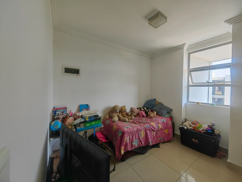 A bedroom featuring tiled flooring, a large aluminium window, and a ceiling cornice, providing a functional space with natural light.