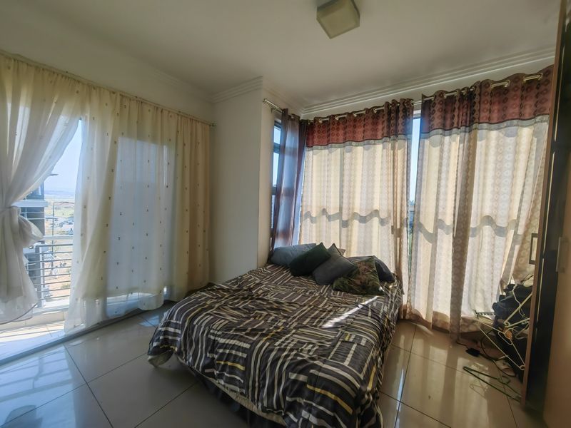A bright bedroom featuring large windows, tiled flooring, and direct access to a balcony through a sliding glass door.