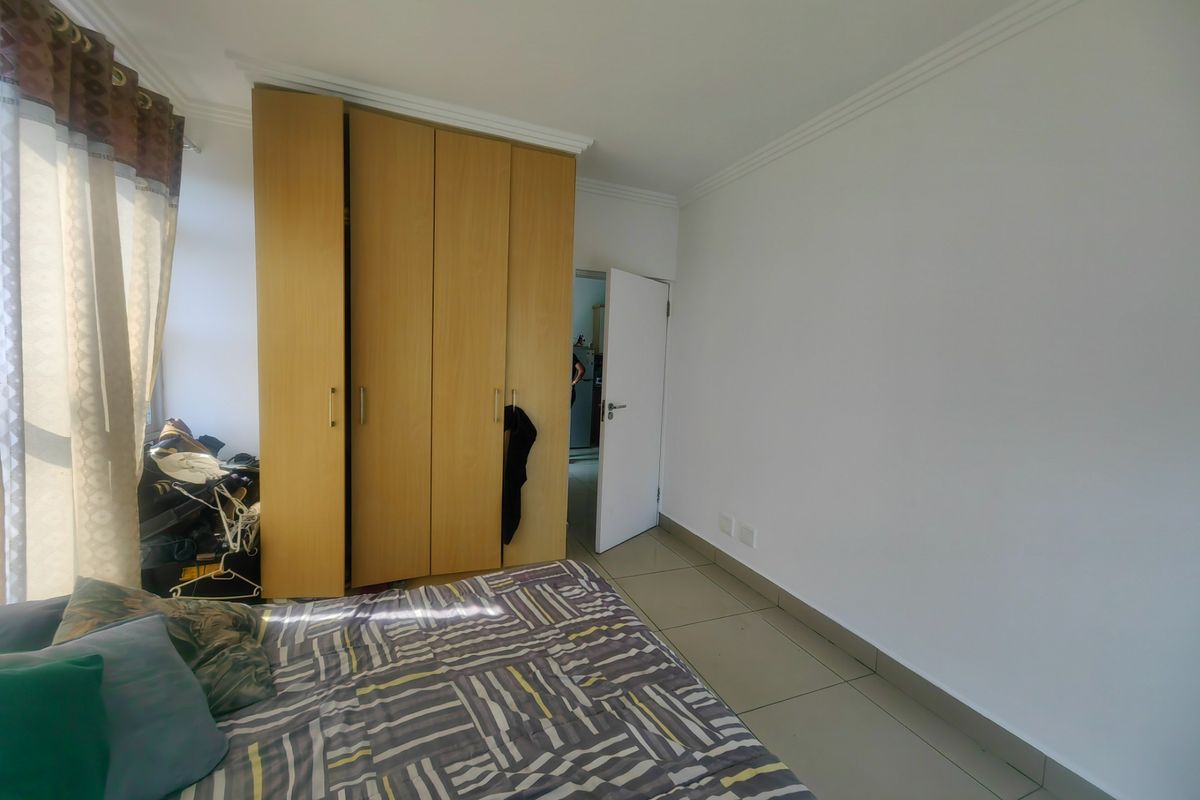 A bedroom featuring built-in wooden cupboards, tiled flooring, and neutral wall finishes, providing a functional and well-lit living space.