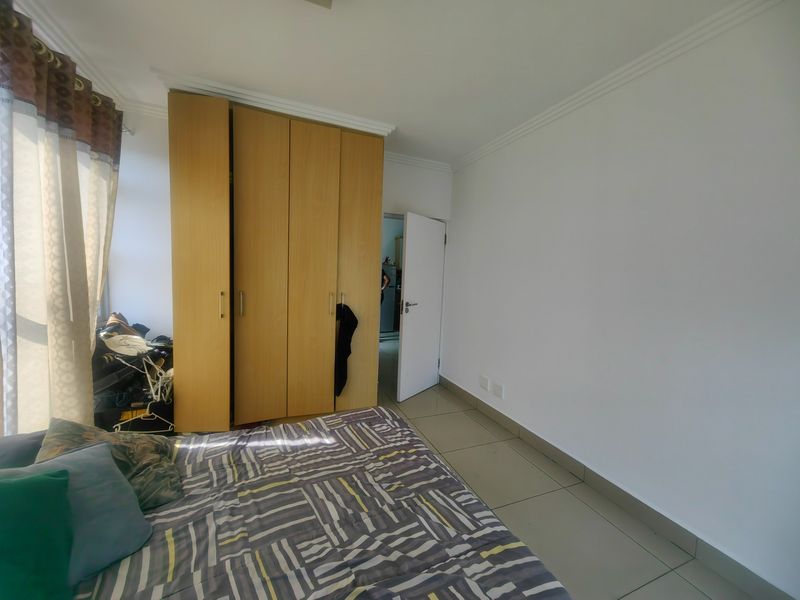A bedroom featuring built-in wooden cupboards, tiled flooring, and neutral wall finishes, providing a functional and well-lit living space.
