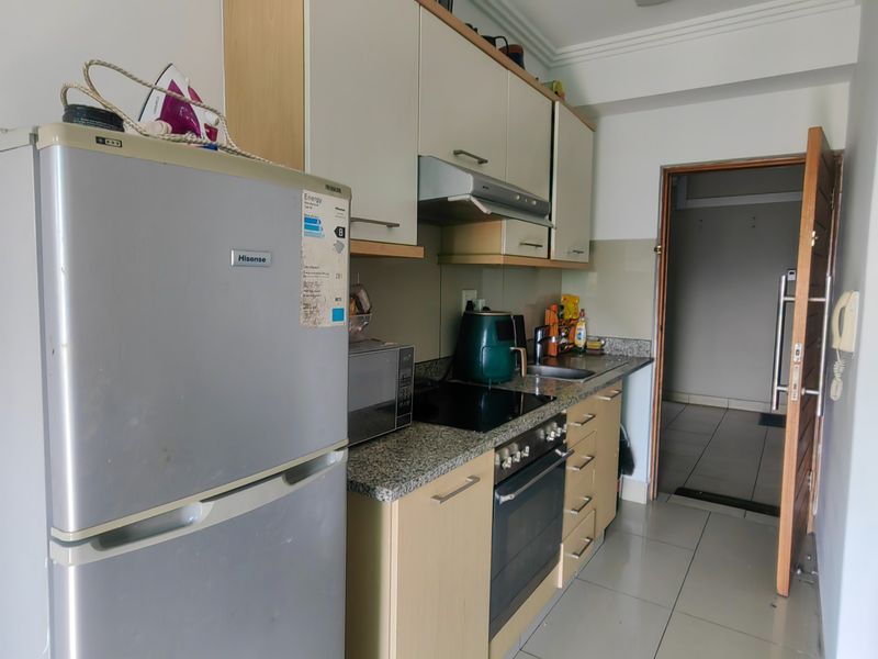 A functional kitchen featuring built-in cabinetry, granite countertops, an electric hob, an oven, and an extractor fan, with tiled flooring throughout.