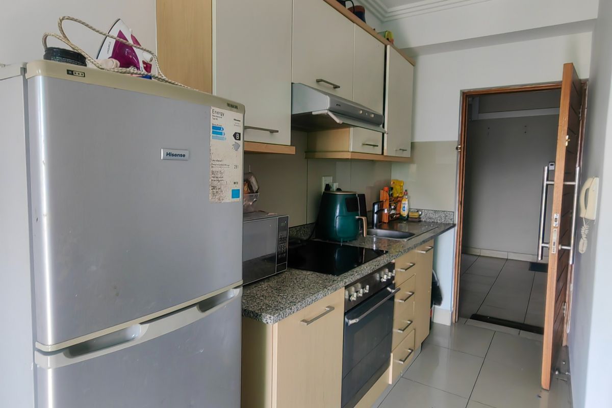 A functional kitchen featuring built-in cabinetry, granite countertops, an electric hob, an oven, and an extractor fan, with tiled flooring throughout.