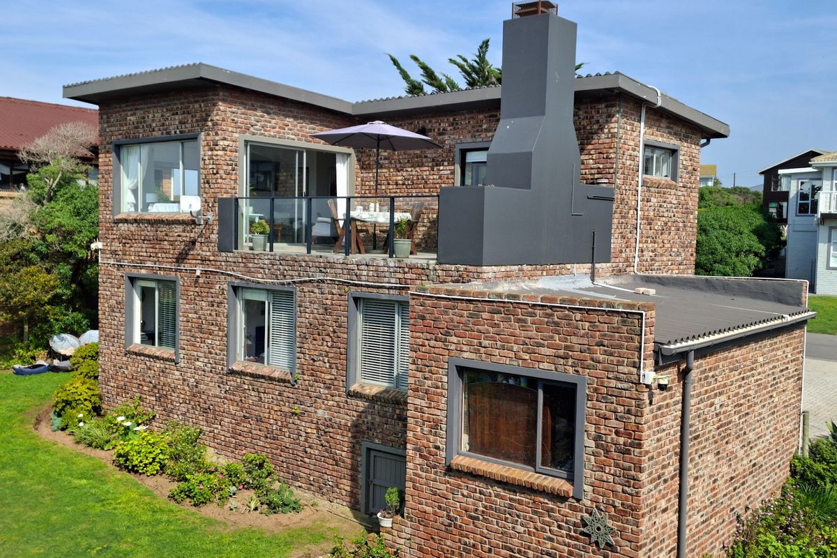 Rear view of a multi-story exposed brick house featuring a balcony with glass balustrade, external chimney, and large sliding doors.