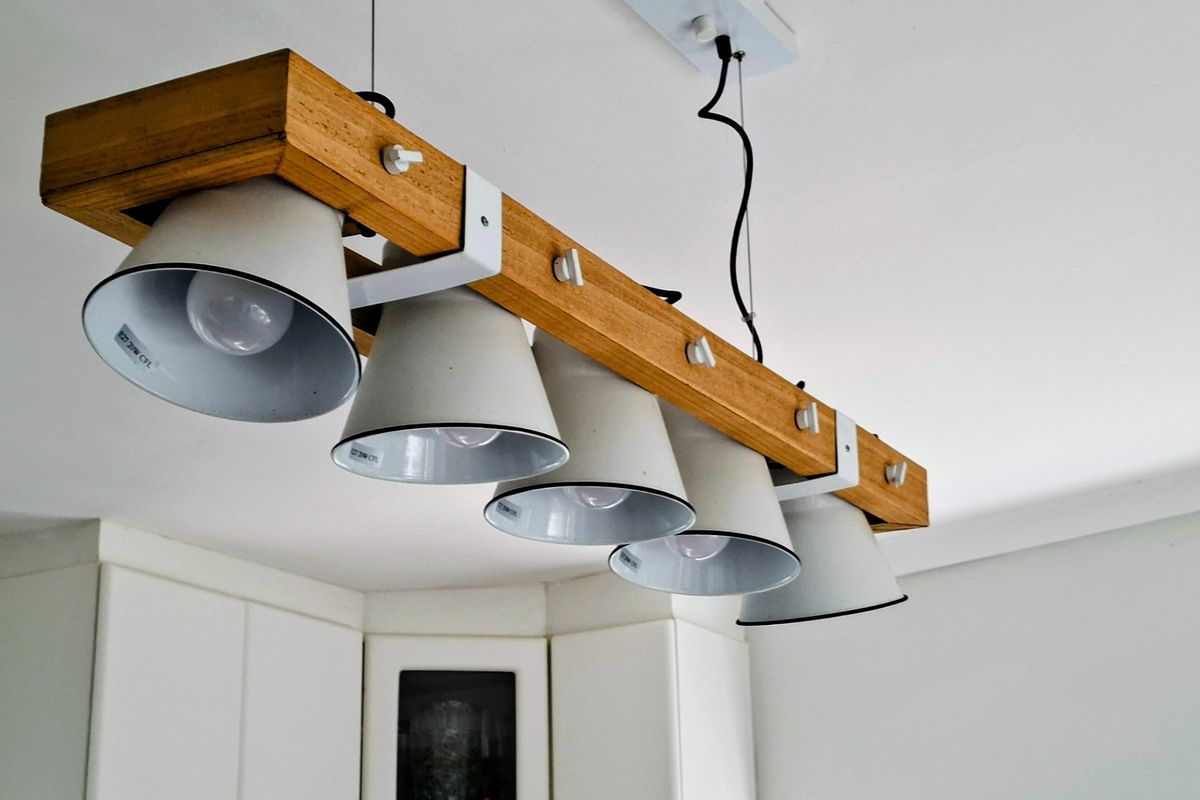 A close-up view of a modern wooden and white metal pendant light fixture installed above kitchen cabinetry.