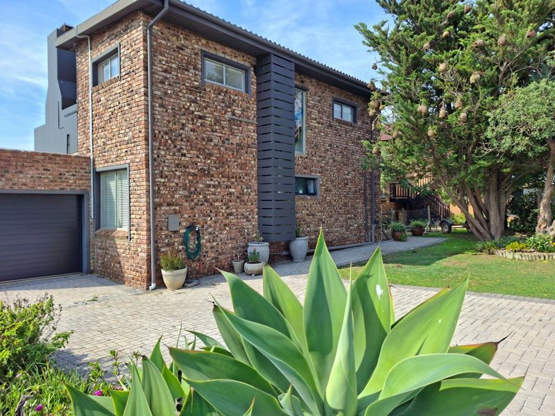A well-maintained double-story face brick house featuring a paved driveway, integrated garage, and established garden surroundings.