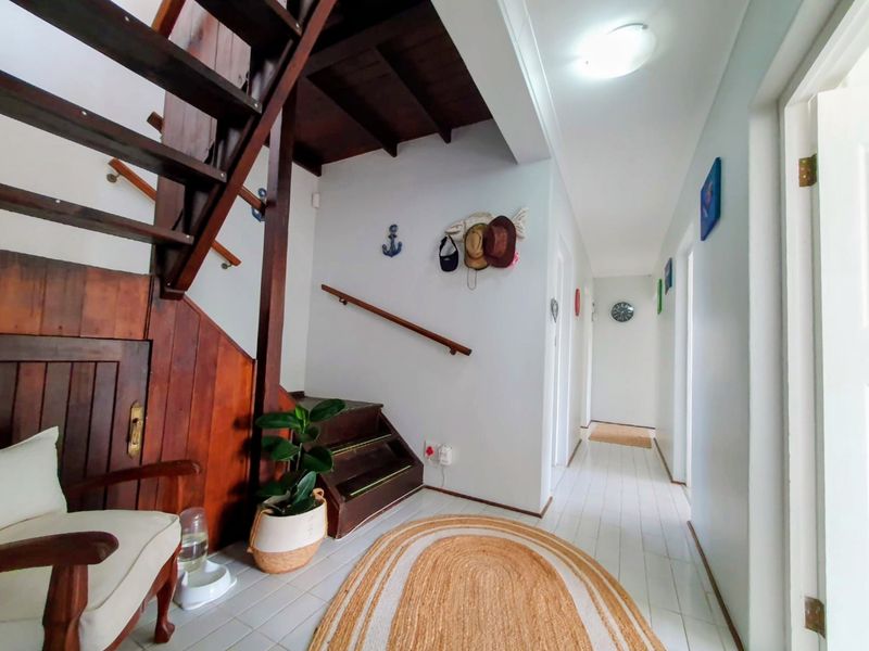 A bright hallway featuring a timber staircase with exposed wooden ceiling beams and tiled flooring, providing access to various rooms in the home.