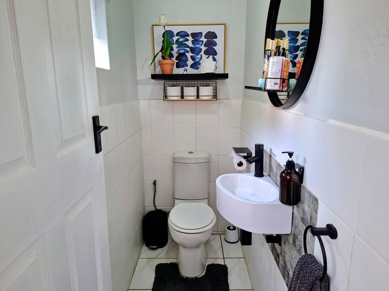 A compact, well-maintained guest bathroom featuring white wall tiles, a wall-mounted basin, and modern black fixtures.