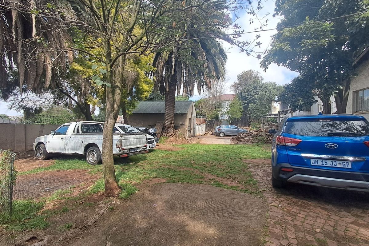 A rear exterior view of the property featuring a large garden area, paved driveway, and perimeter walling.