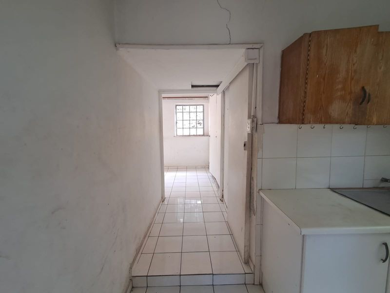 A narrow hallway with tiled flooring leading to an adjacent room, featuring basic built-in cabinetry and visible structural wall cracking.