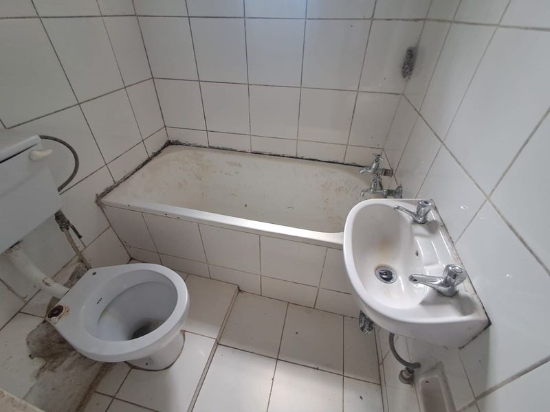 A dated bathroom featuring a bathtub, wall-mounted basin, and toilet, requiring significant refurbishment and modernization of fixtures and finishes.