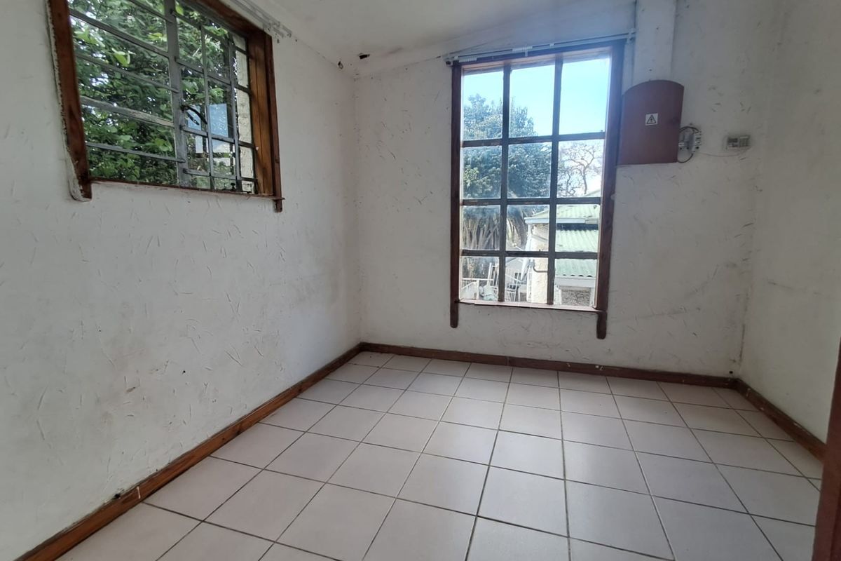 An empty bedroom featuring tiled flooring, timber-framed windows with security bars, and an exposed electrical distribution board, requiring cosmetic renovation.