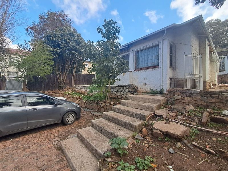 Front exterior view of the house featuring a paved driveway, concrete stairs, and stone retaining walls with visible signs of wear and weathering.