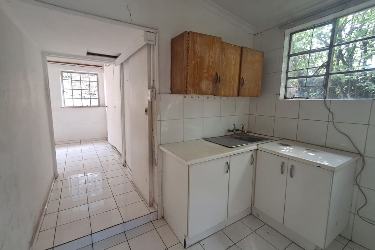 A dated kitchen area featuring basic cabinetry, a stainless steel sink, and tiled flooring, requiring renovation to modernize the space.