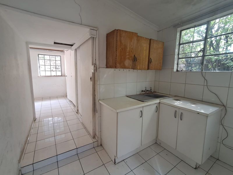 A dated kitchen area featuring basic cabinetry, a stainless steel sink, and tiled flooring, requiring renovation to modernize the space.