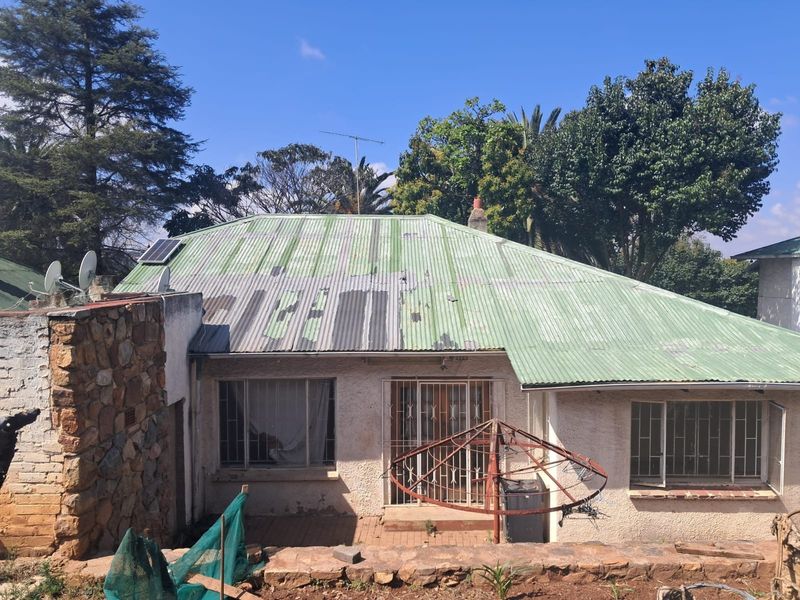 Rear view of the house featuring a corrugated metal roof with visible wear, stone cladding accents, and security bars on the windows.