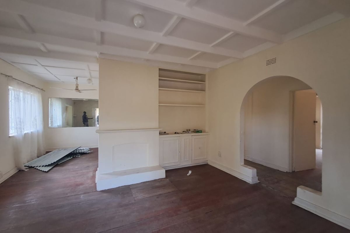 Spacious living area featuring a coffered ceiling, built-in cabinetry, a fireplace mantle, and an arched entryway, with original timber flooring throughout.