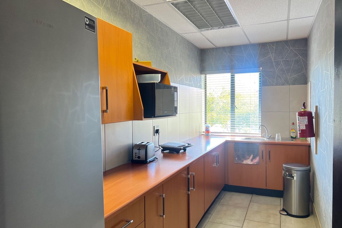 A functional commercial kitchenette featuring laminate cabinetry, tiled backsplash, stainless steel sink, and drop ceiling lighting.