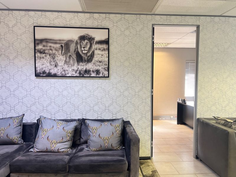 A professional office space featuring patterned wallpaper, tiled flooring, and a suspended ceiling, with an open doorway leading to an adjacent workspace.