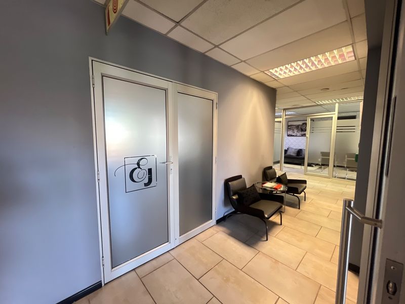 A professional commercial hallway featuring ceramic tiled flooring, suspended ceilings with recessed lighting, and frosted glass double doors leading to an office suite.