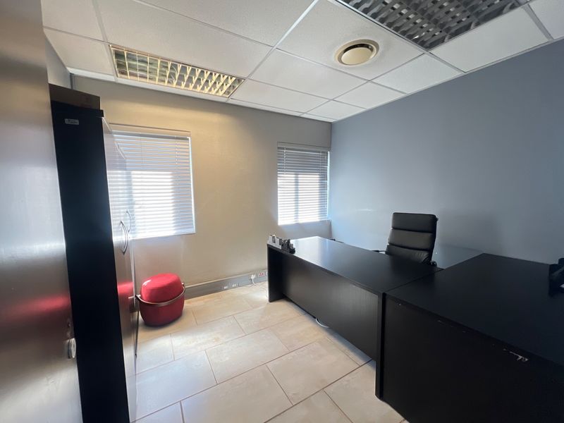 A functional commercial office space featuring tiled flooring, suspended ceilings with recessed lighting, and dual windows with fitted venetian blinds.