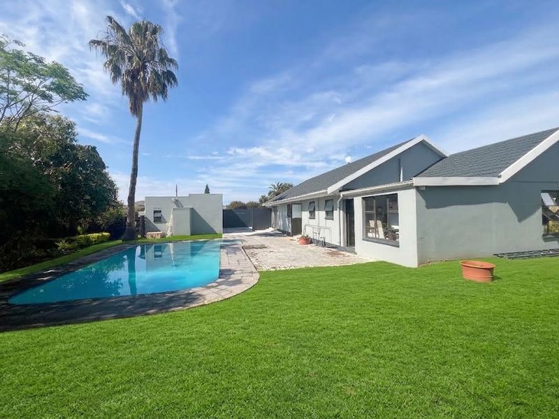 Rear exterior view featuring a swimming pool, paved patio area, and a well-maintained lawn set against the house structure.