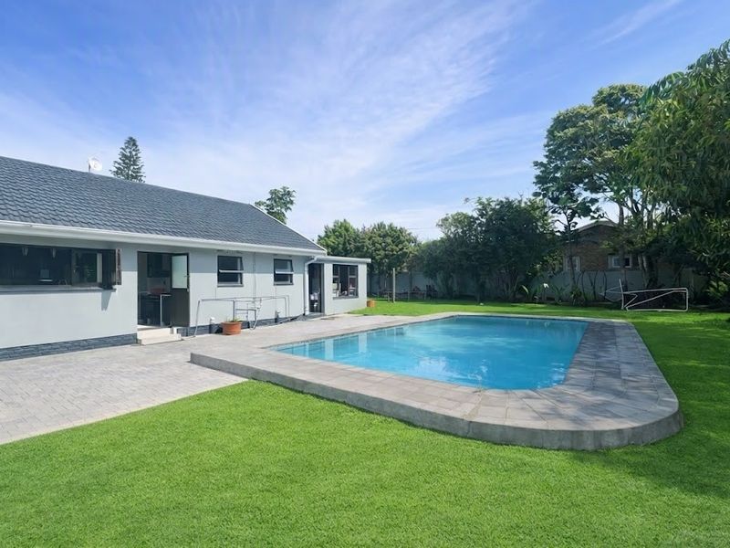 A well-maintained rear garden featuring a swimming pool with a paved surround, adjacent to the main house structure with a tiled roof.