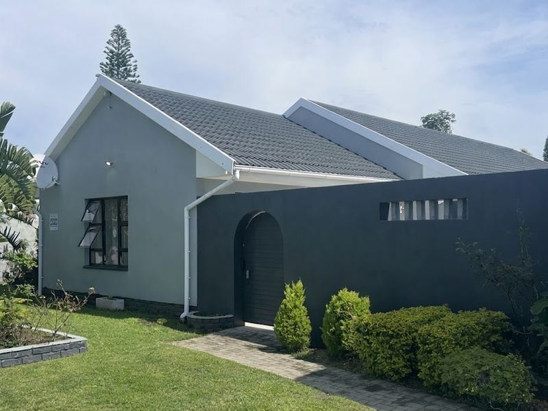 A well-maintained single-story home featuring a modern grey facade, tiled roof, and a private arched entrance gate with a paved walkway.