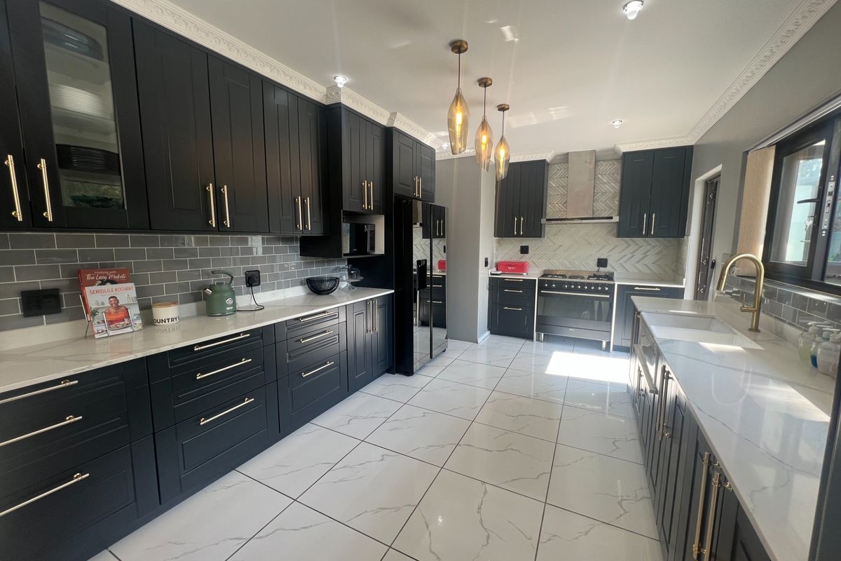 Modern, high-end kitchen featuring dark shaker cabinetry, quartz countertops, subway tile backsplash, premium gas range, and elegant brass fixtures with large-format floor tiles.