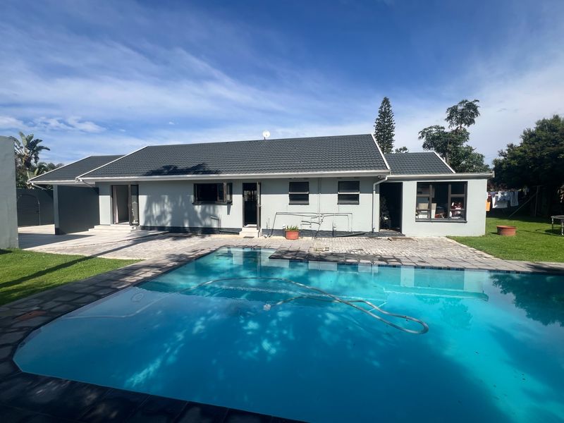 Rear view of the property featuring a well-maintained swimming pool, paved patio area, and a clean exterior facade with a tiled roof.
