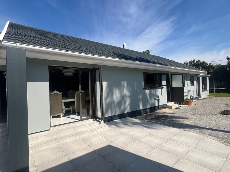 Rear view of the property featuring a paved patio area, bi-fold doors leading into the living space, and a well-maintained tiled roof.