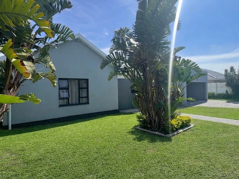 Front view of a well-maintained house featuring a neat lawn, paved driveway, garage, and established garden landscaping.