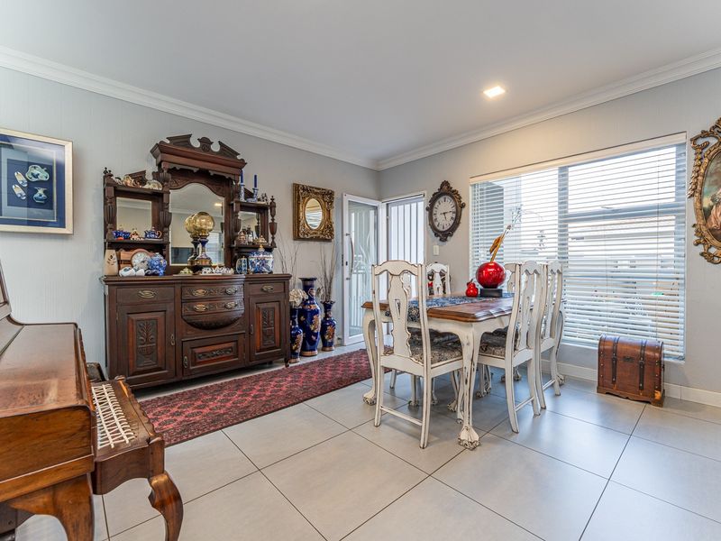 A well-maintained dining room featuring neutral tiled flooring, recessed lighting, and large windows with venetian blinds, providing a bright and functional space.