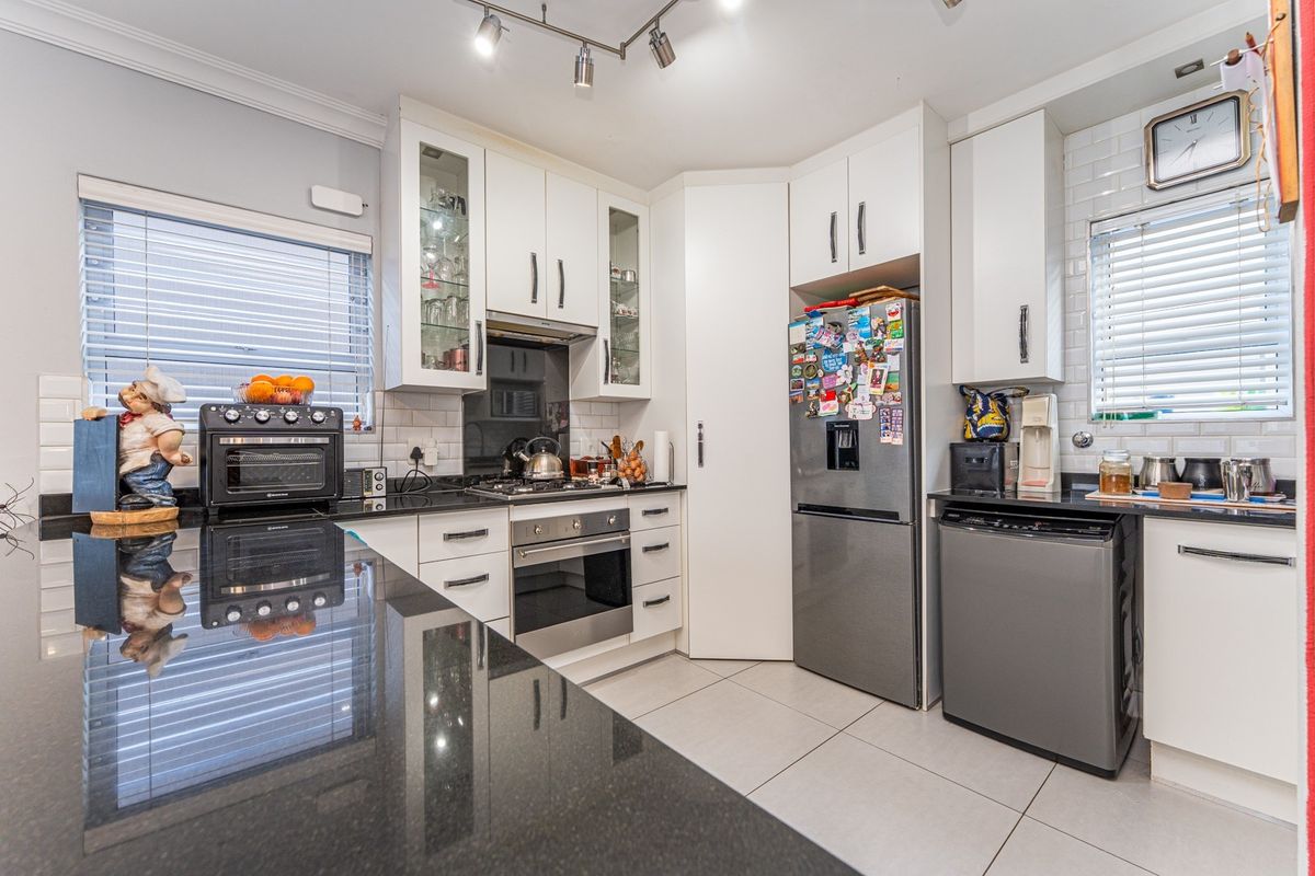 Modern kitchen featuring white cabinetry, black granite countertops, subway tile backsplash, built-in oven, gas hob, and tiled flooring.