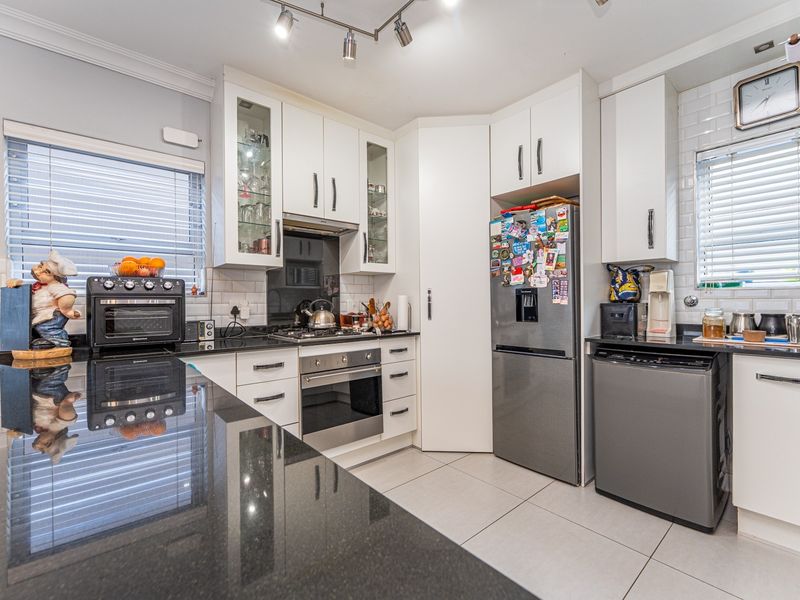 Modern kitchen featuring white cabinetry, black granite countertops, subway tile backsplash, built-in oven, gas hob, and tiled flooring.