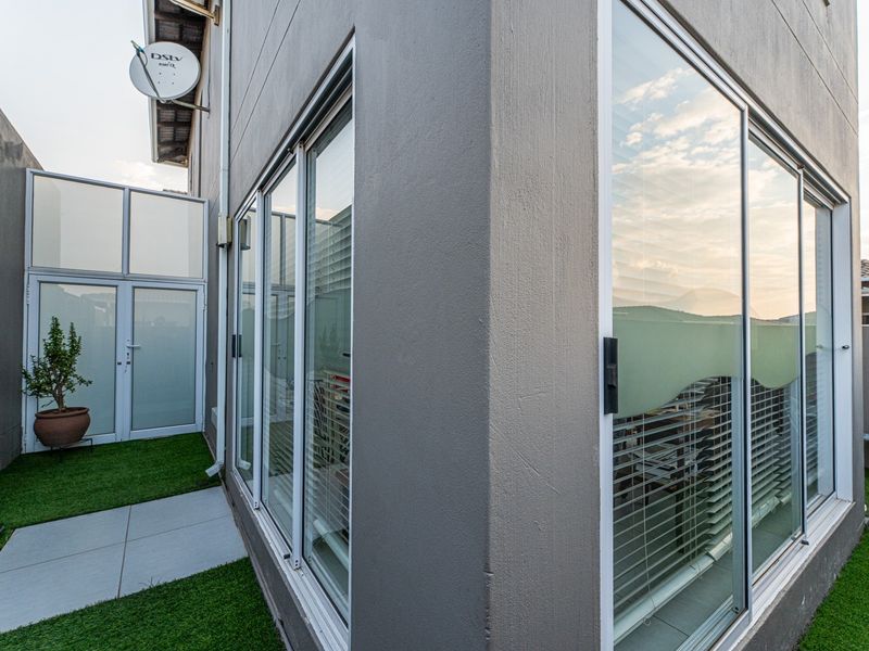A view of the rear exterior of the townhouse featuring sliding glass doors, modern grey facade, and a small paved area with artificial grass.