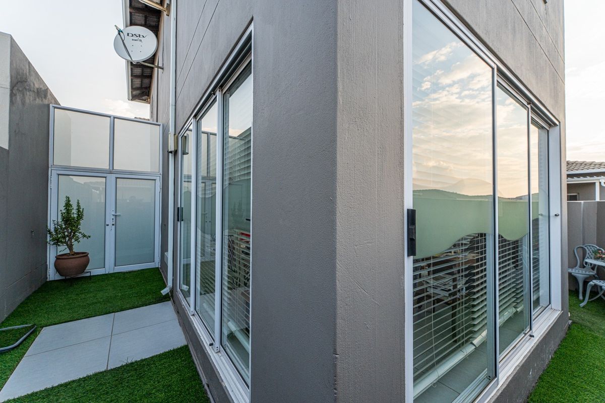 A view of the rear exterior of the townhouse featuring sliding glass doors, modern grey facade, and a small paved area with artificial grass.