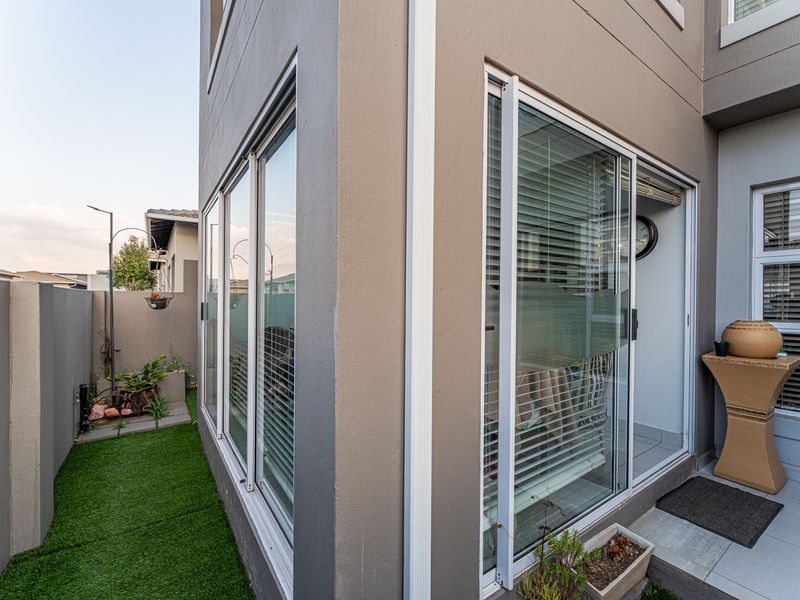 Rear exterior view of the townhouse featuring a tiled patio area, sliding glass doors, and a small garden space with artificial turf.