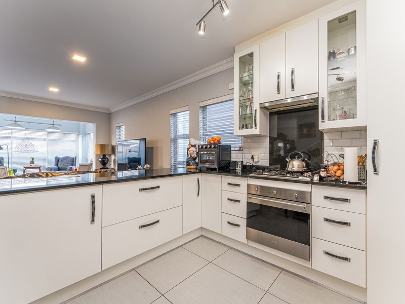 Modern open-plan kitchen featuring sleek white cabinetry, granite countertops, gas hob, and integrated oven, seamlessly flowing into the adjacent living area.