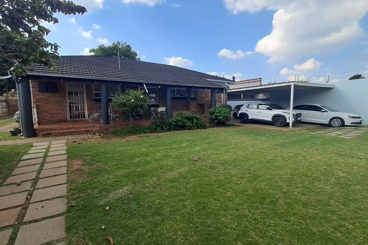 Rear view of a brick house featuring a covered patio, a well-maintained lawn, a paved walkway, and a double carport.